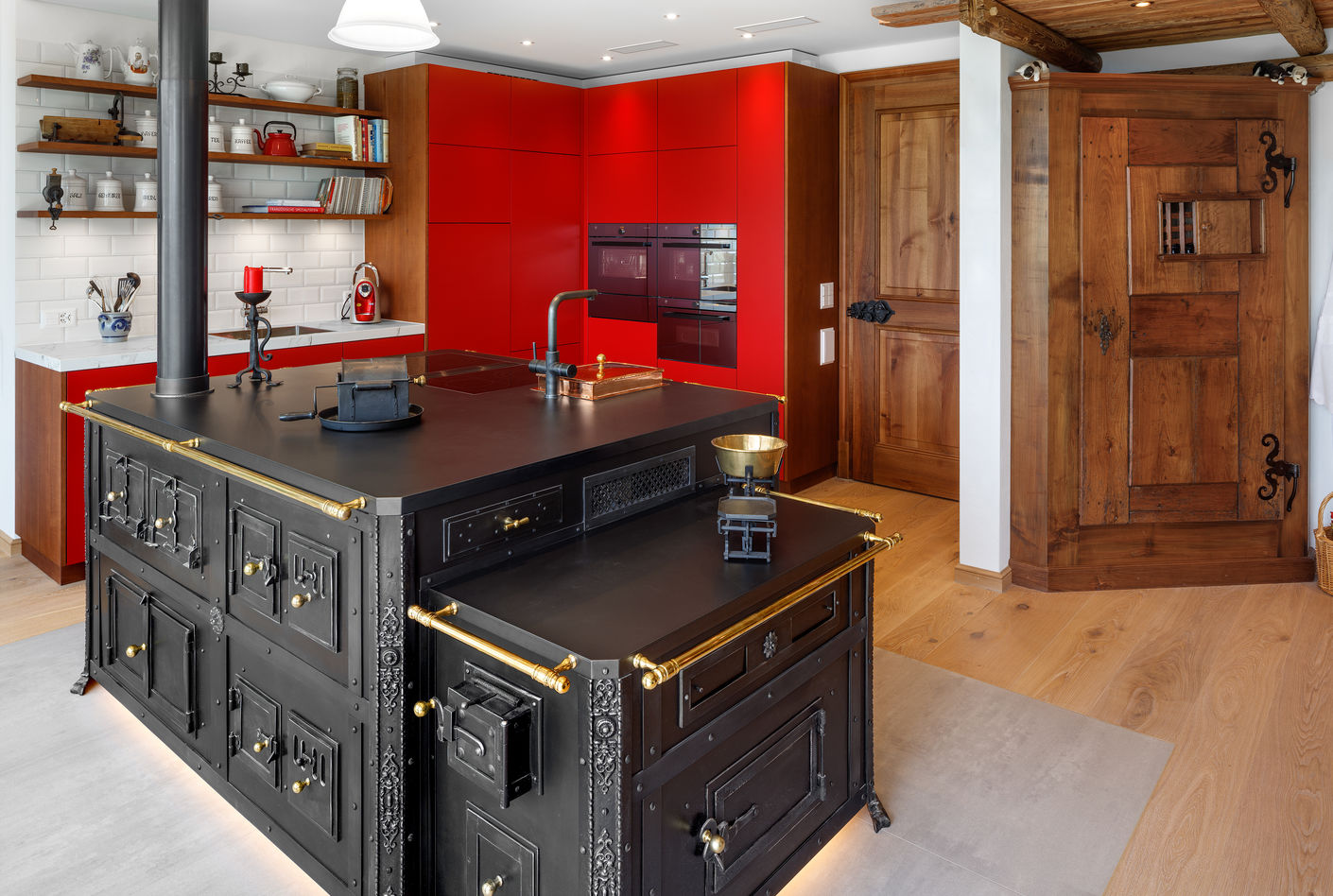 Die Romantik der Vergangenheit kontrastiert mit den roten Küchenfronten. Die Regale sind wie die Türe aus Nussbaumholz hergestellt, passend zur hölzernen Deckenverkleidung.
